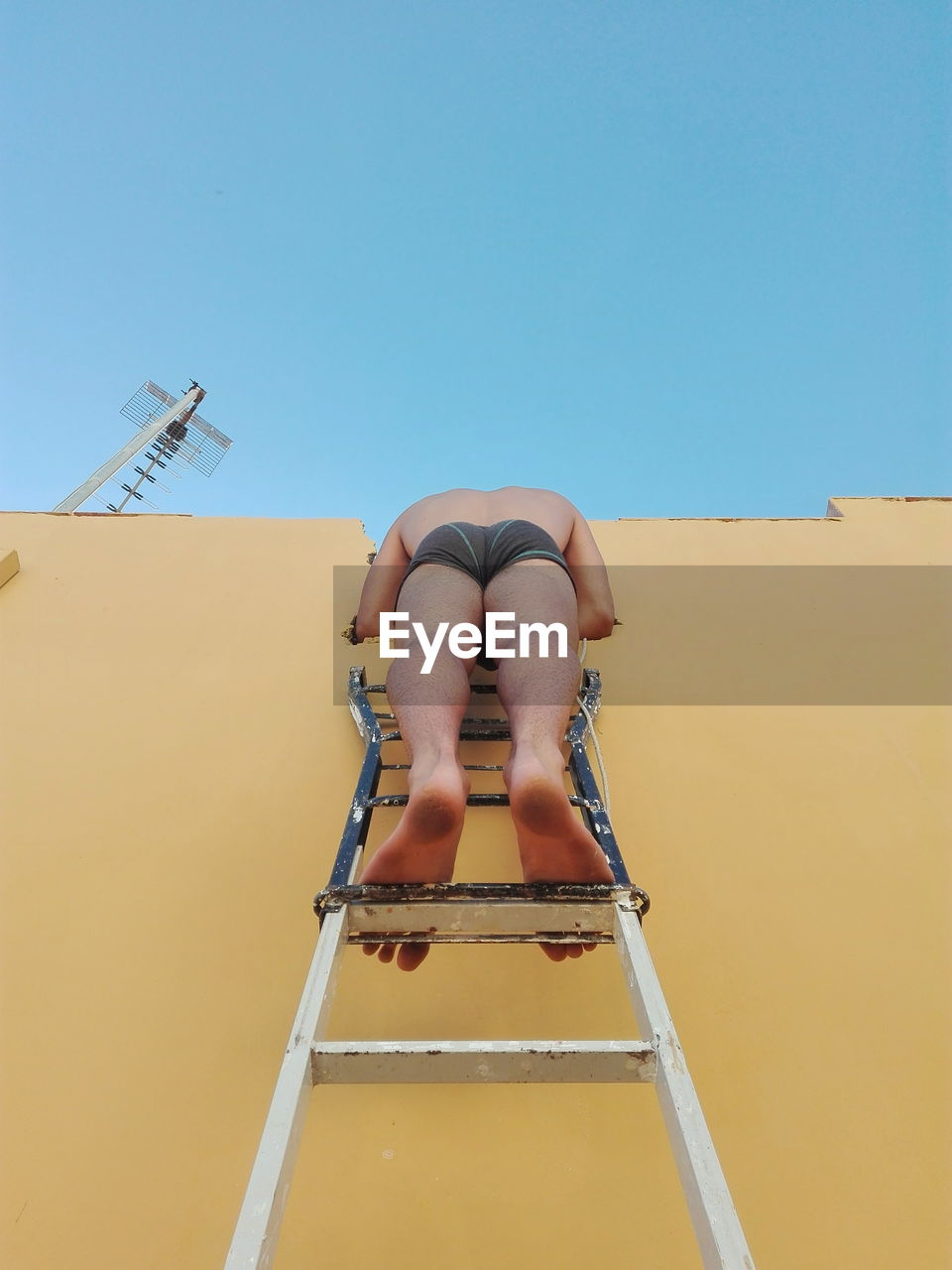 Low section of shirtless man on ladder against clear sky