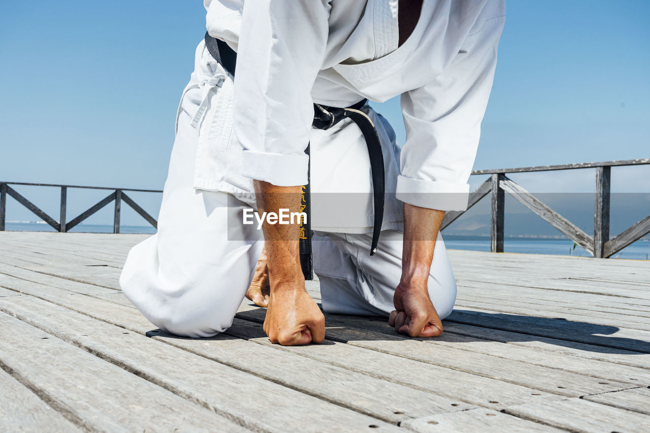 Karate man leaning with clenched fists on wooden platform