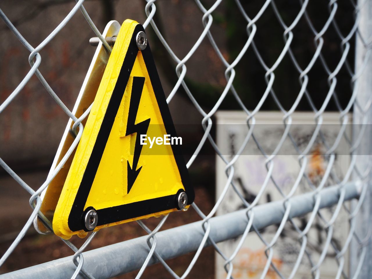Close-up of high voltage sign board on chainlink fence