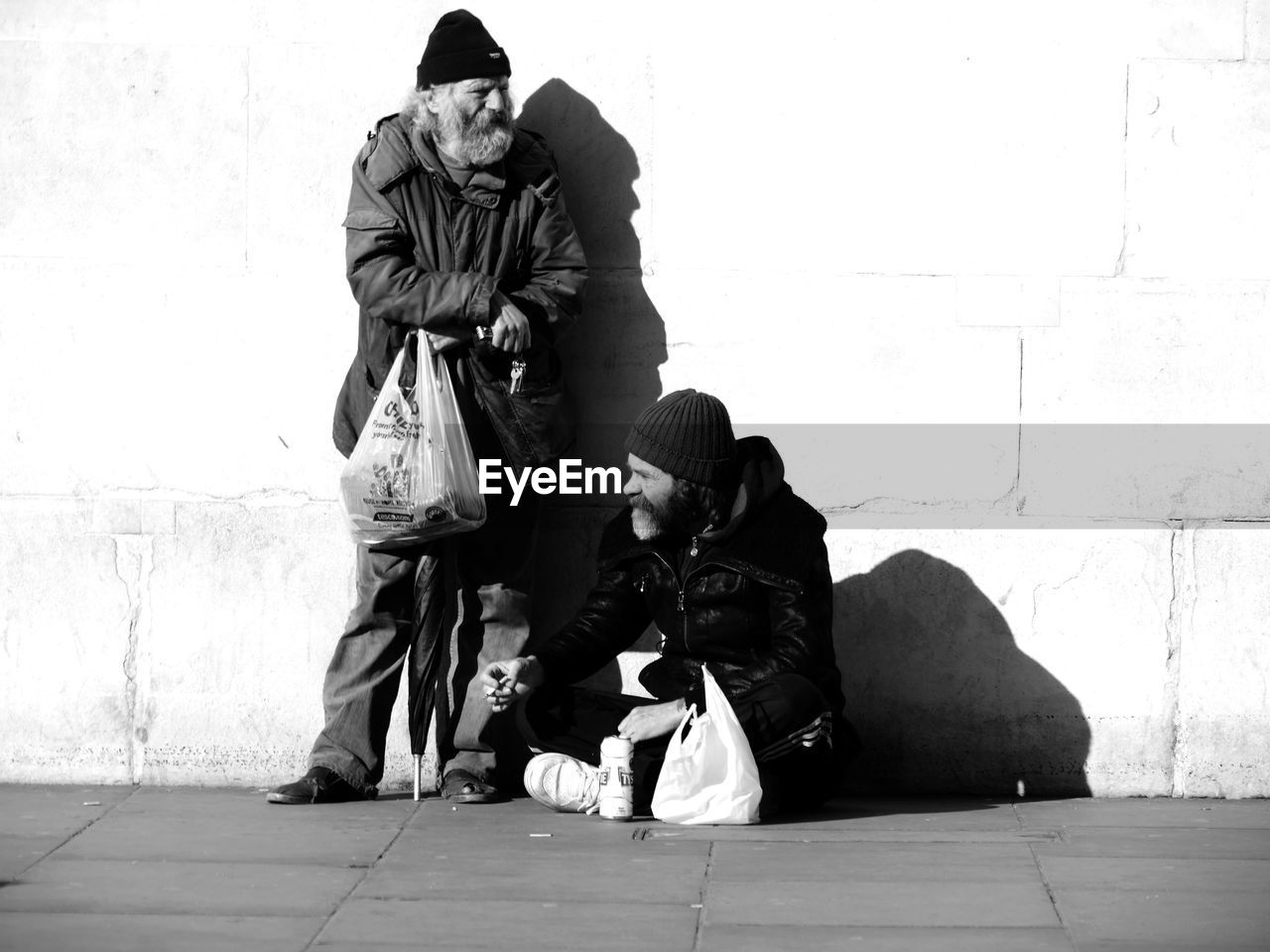 Senior beggars on street against wall during sunny day