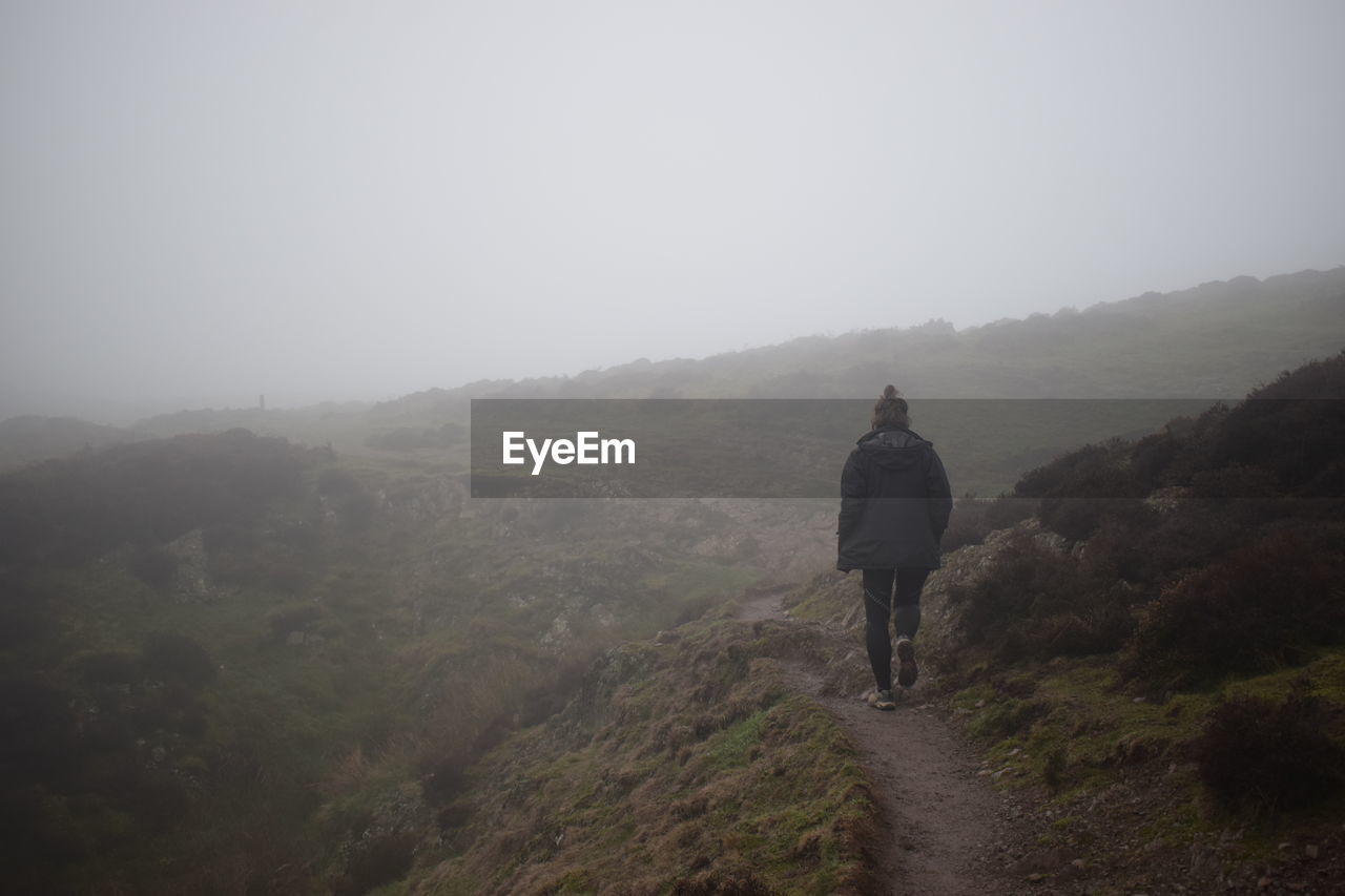 Rear view of hiker walking on mountain against sky during foggy weather