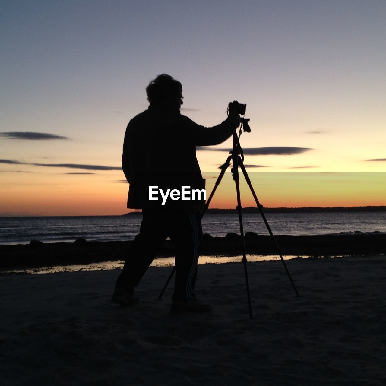 Silhouette man photographing sea against sky