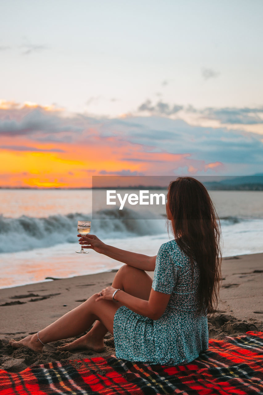 Woman sitting on beach against sky during sunset