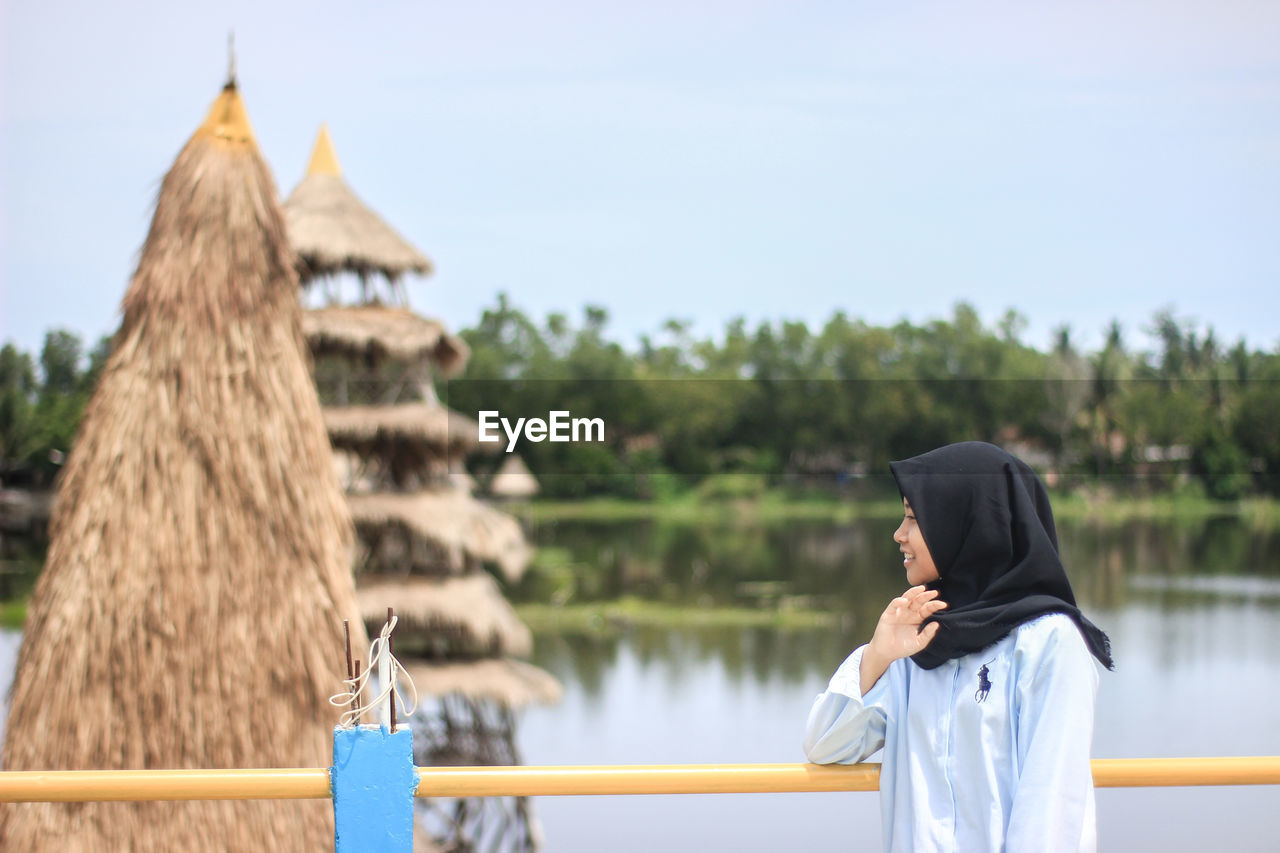 Side view of woman standing by railing and lake against sky