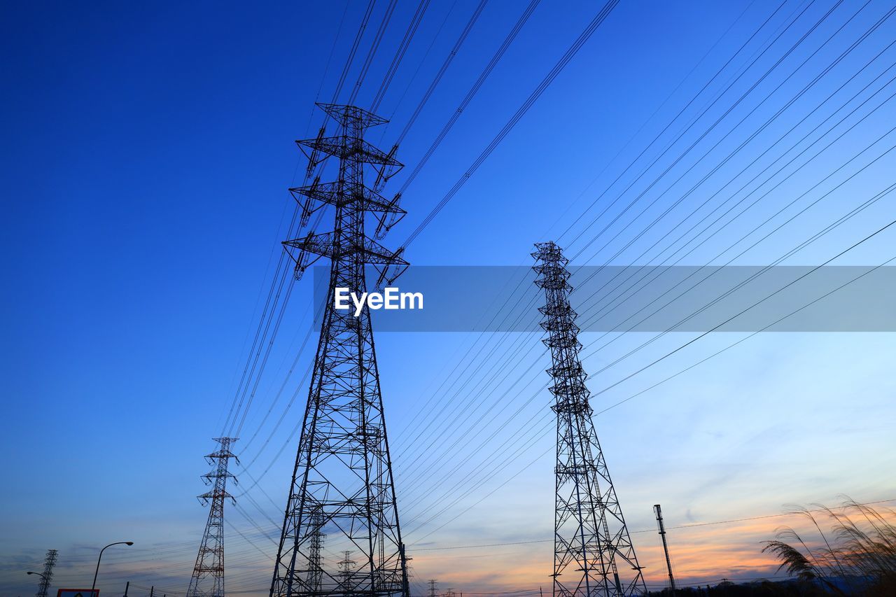 Low angle view of electricity pylons against clear blue sky during sunset