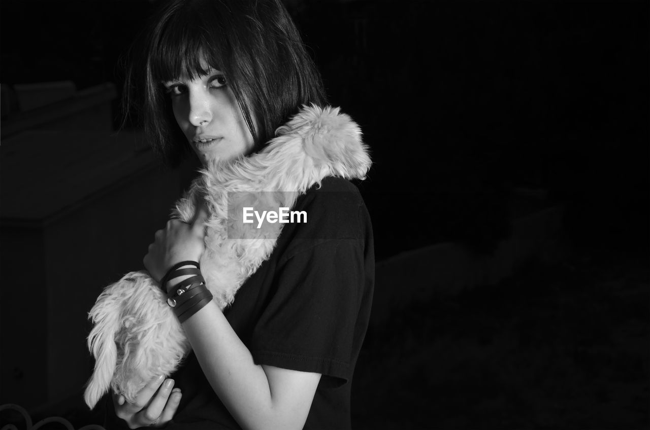 Portrait of woman holding puppy against black background