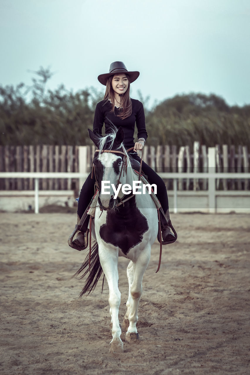 Portrait of woman sitting on horse in ranch against sky