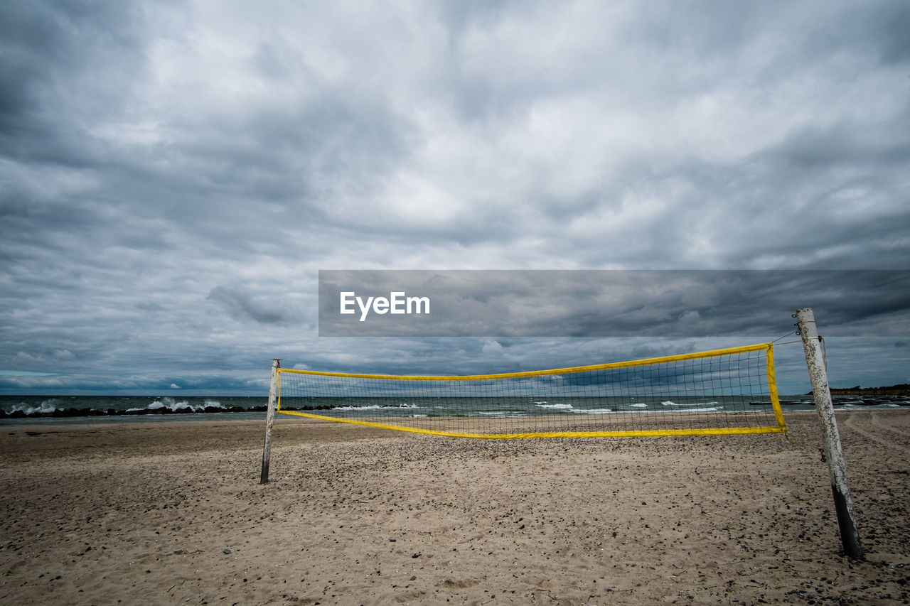 Volleyball net at beach against cloudy sky