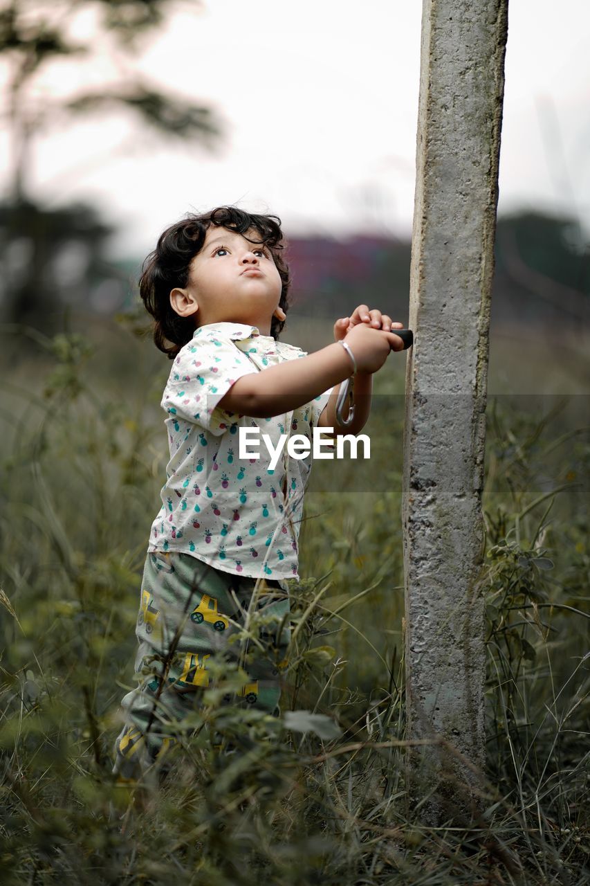 Cute boy standing by tree outdoors