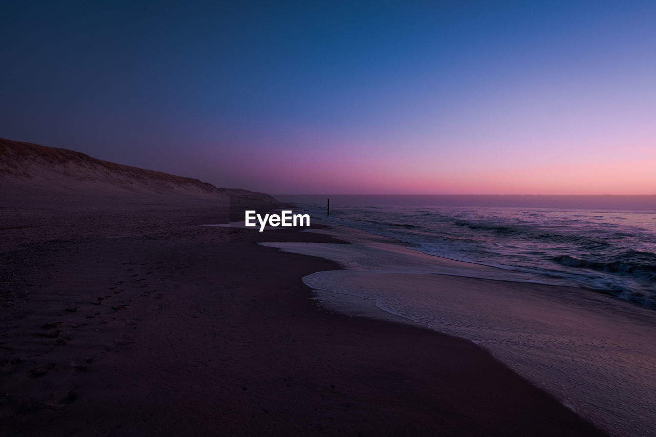 SCENIC VIEW OF BEACH AGAINST SKY AT SUNSET