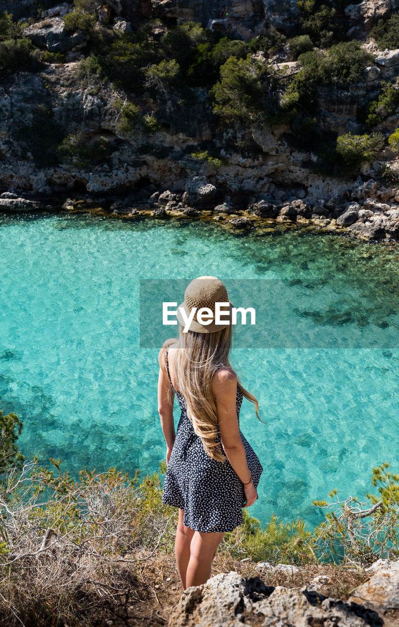 rear view of woman standing on rock by lake