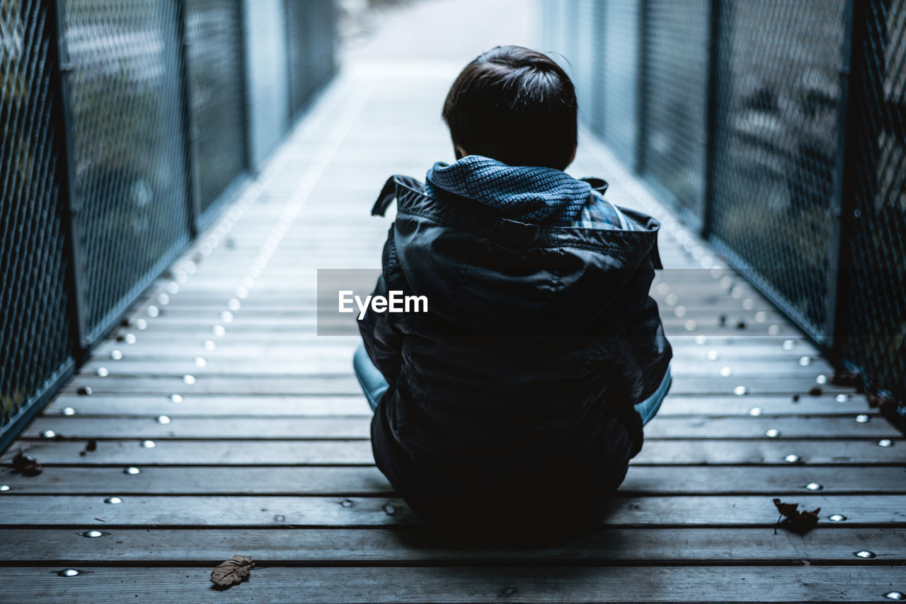 Rear view of boy sitting on bridge