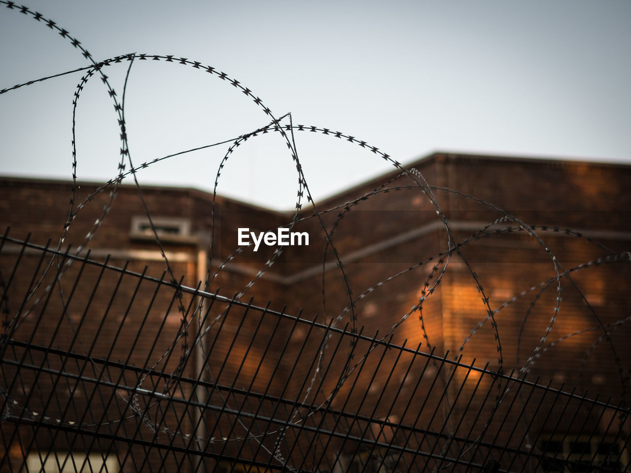Close-up of barbed wire fence against brick building and sky