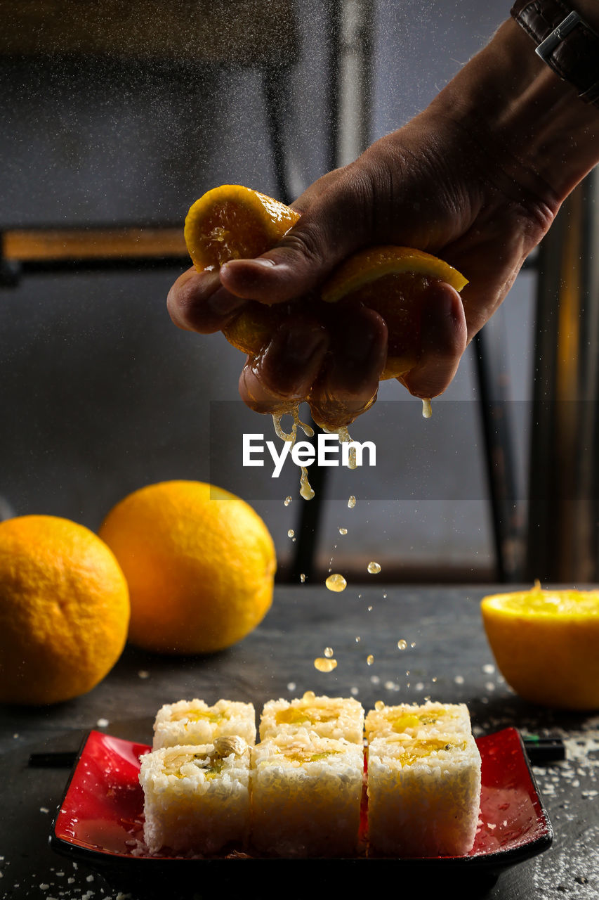 Cropped image of hand crushing orange fruit on sushi in plate