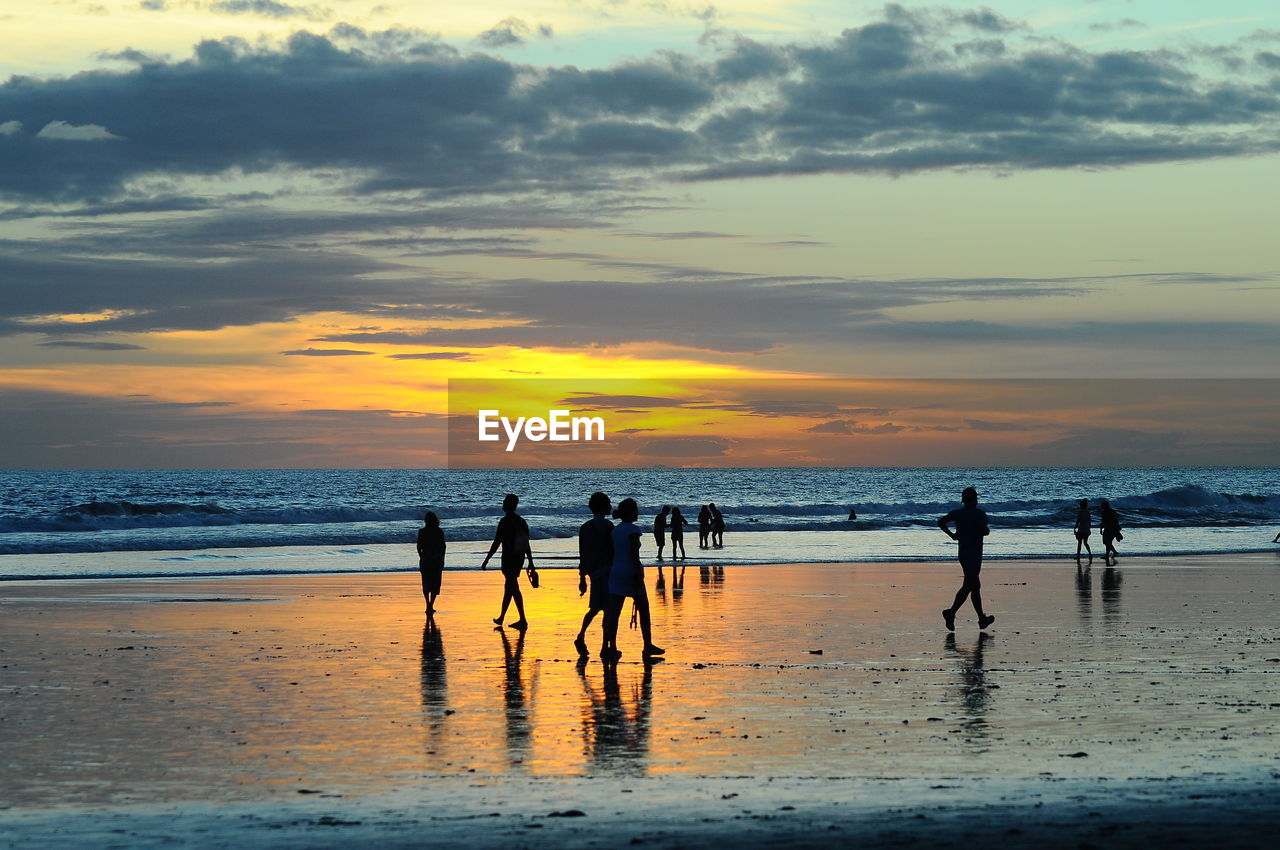 Silhouette people standing on beach against sky during sunset