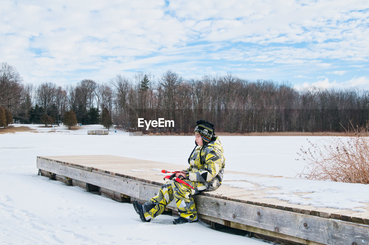 View of child in snowsuit on snow covered landscape against cloudy sky