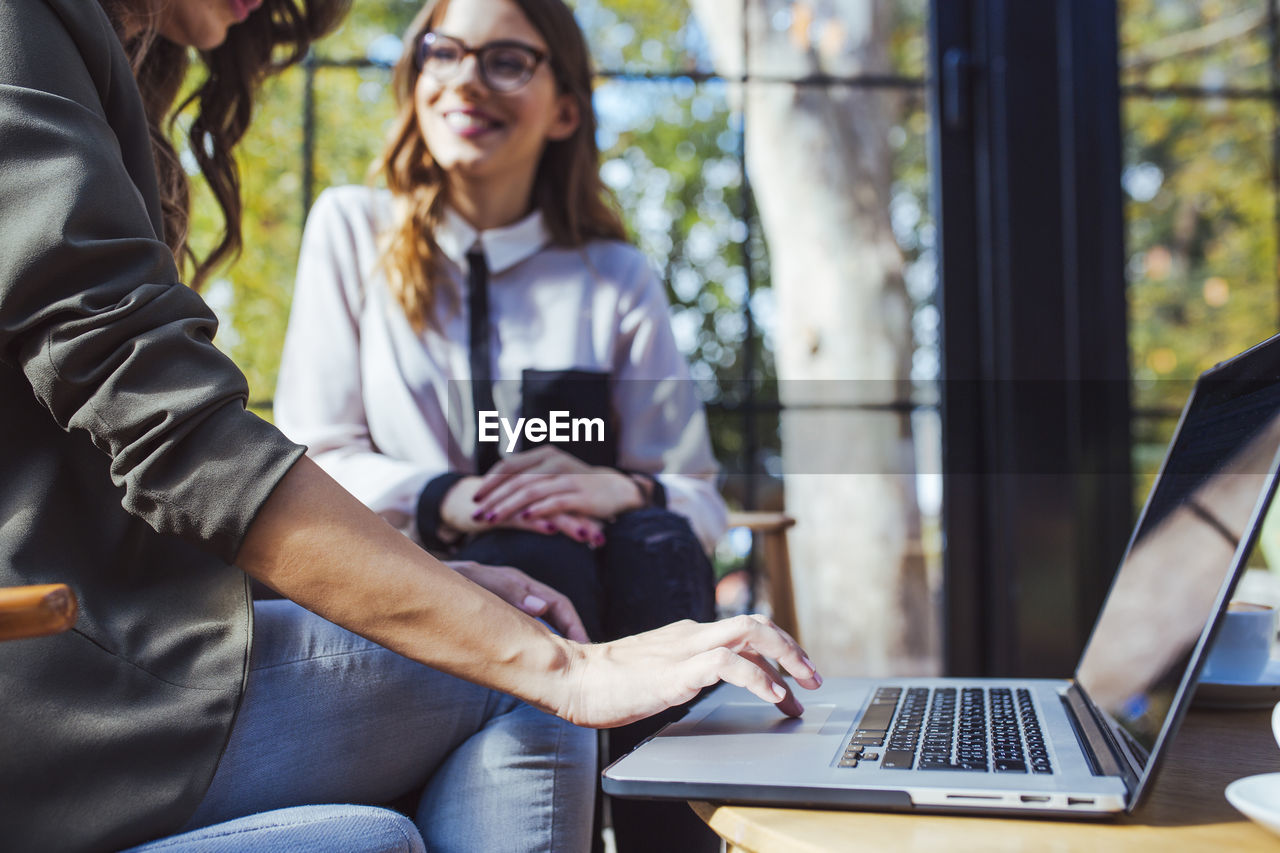 Midsection of woman using laptop computer while sitting with colleague in cafe