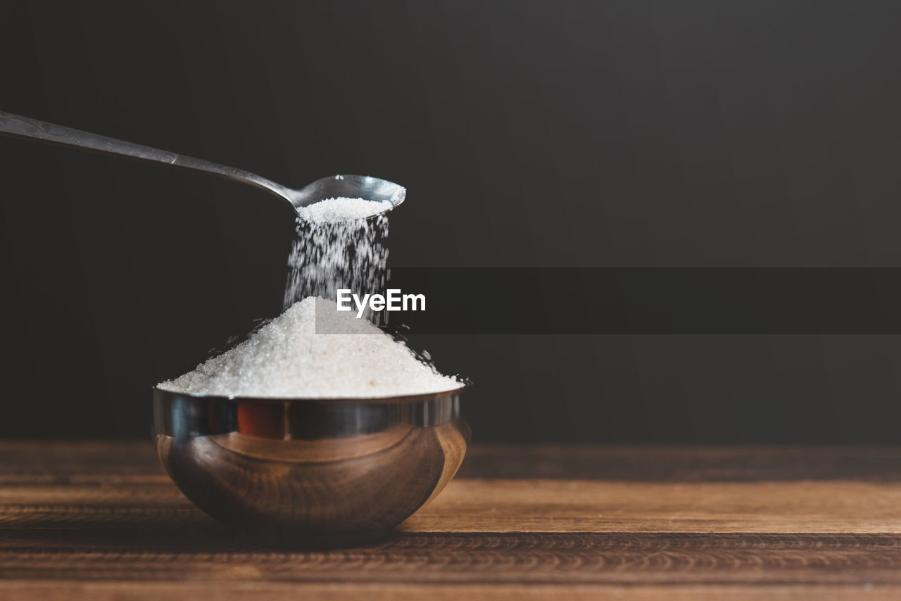 Sugar poured into a steel bowl on a wooden table. concept of unhealthy eating and diabetes