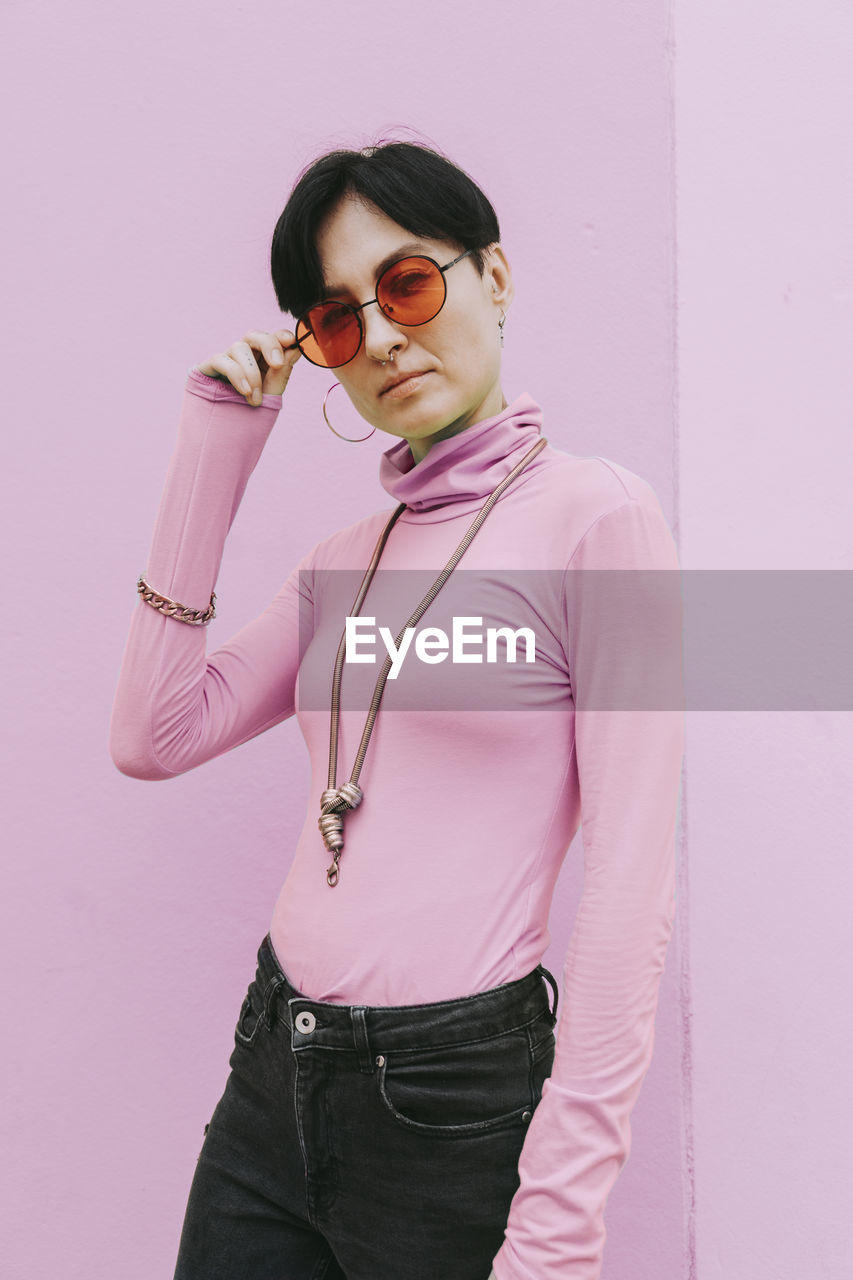 Woman wearing sunglasses standing in front of pink wall