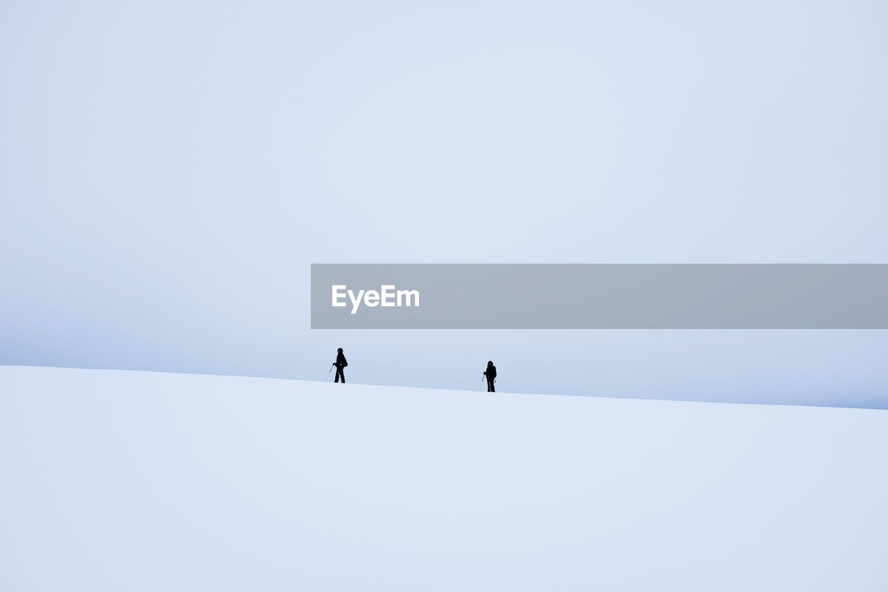 Low angle view of people walking on snow covered landscape against clear sky