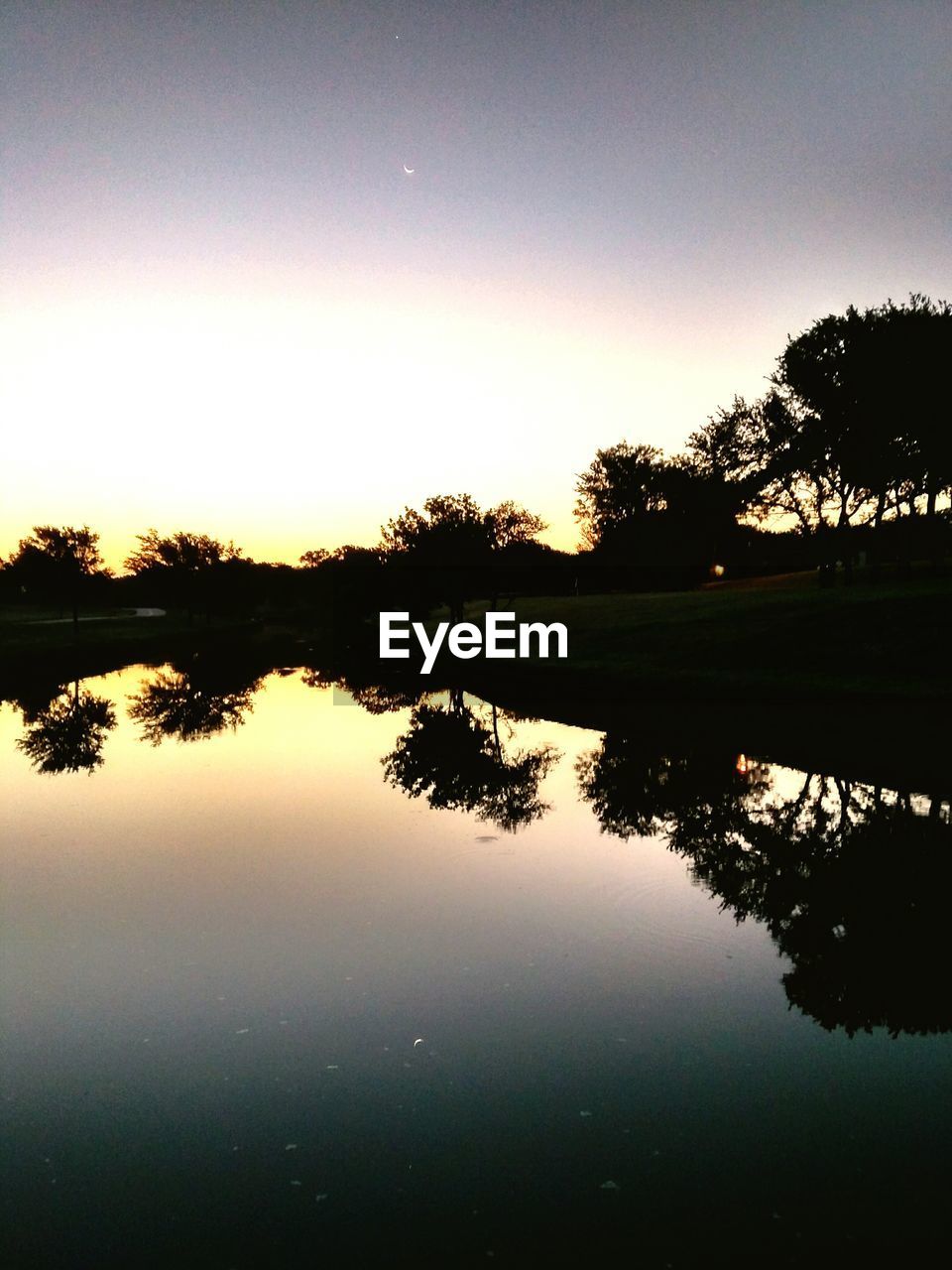 REFLECTION OF SILHOUETTE TREES ON LAKE AGAINST SKY