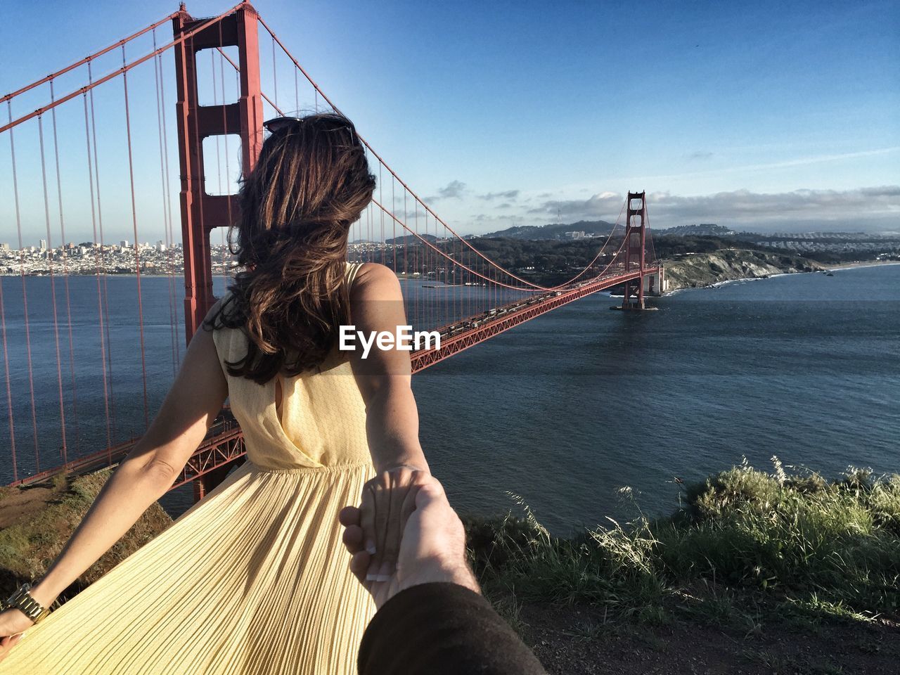 Cropped image of man hand holding woman against golden gate bridge