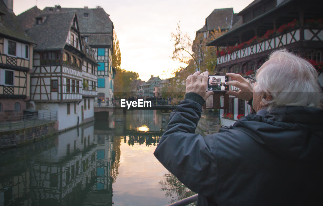 Mature man photographing buildings and canal in city