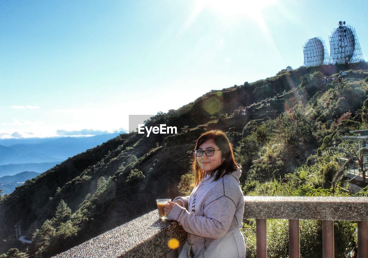 Portrait of young woman with coffee standing against mountains