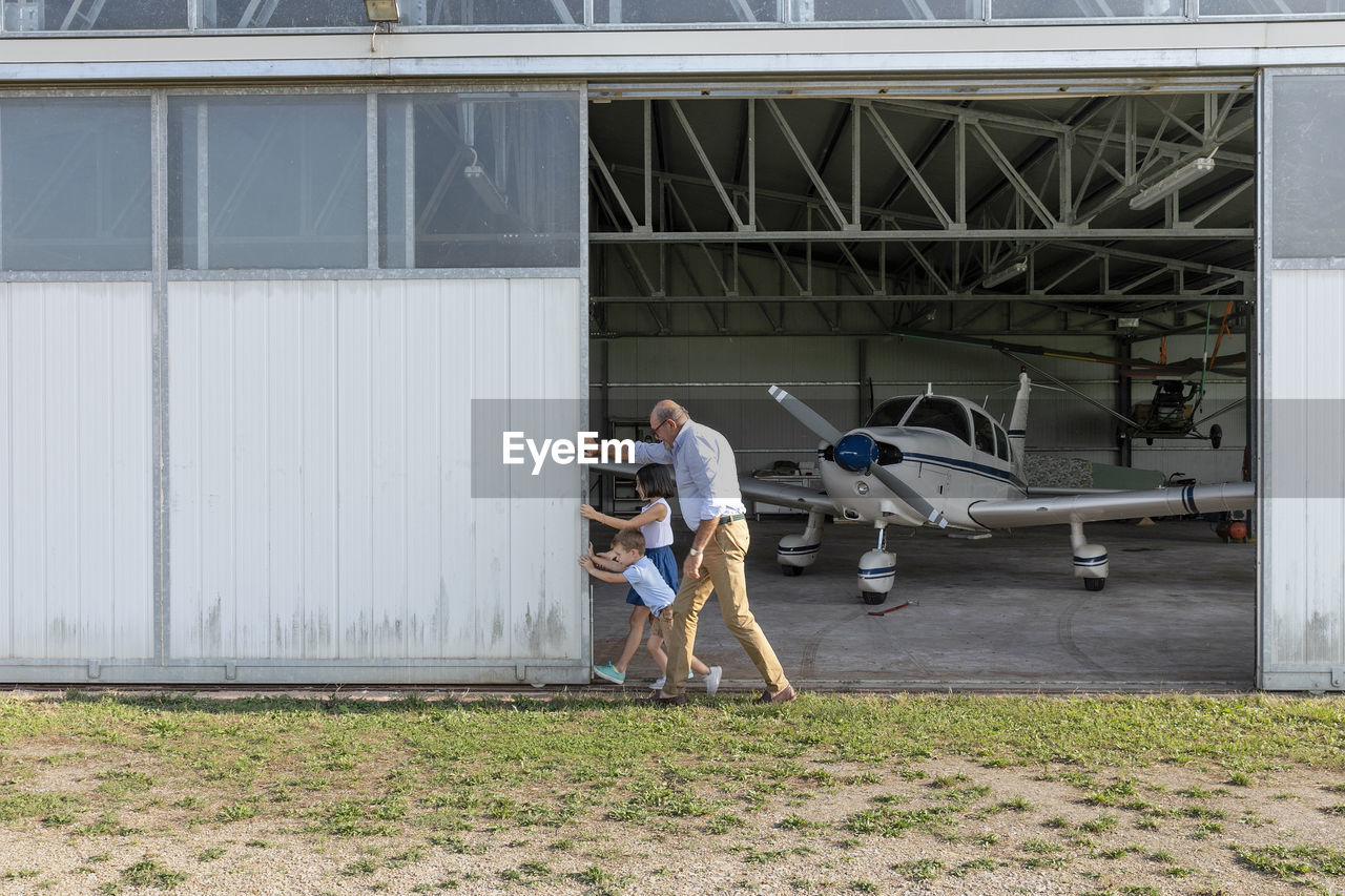 Children and grandfather opening door of airplane hangar