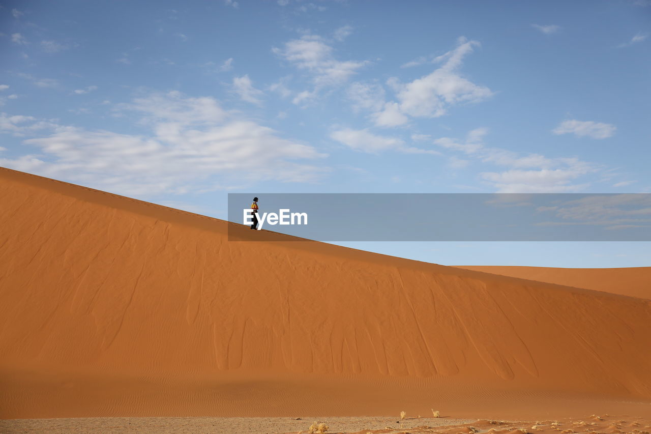 Woman walking on desert against sky