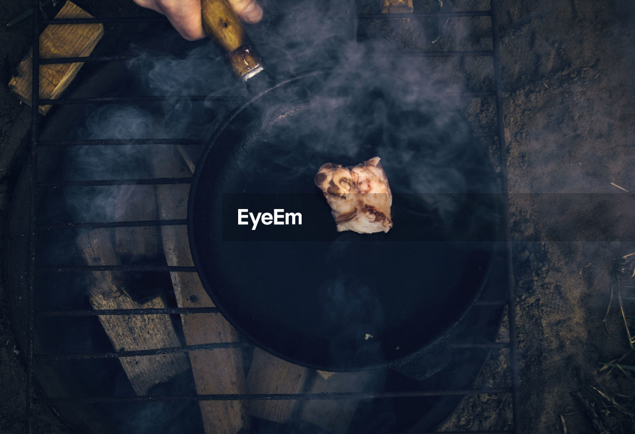 Cropped hand frying meat on wood burning stone