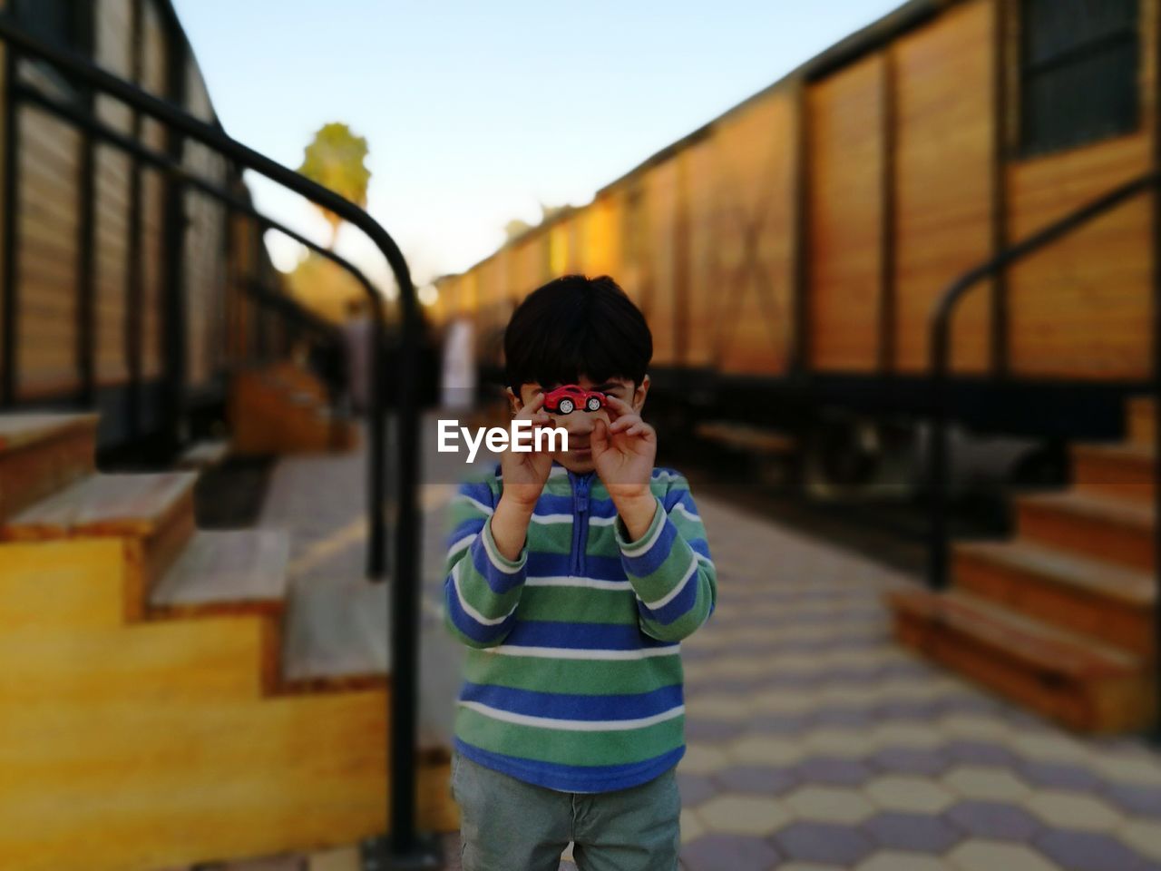 Boy holding toy car amidst freight trains