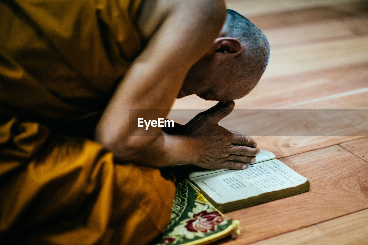 CLOSE-UP OF MAN HOLDING BOOK WHILE SITTING ON WOOD