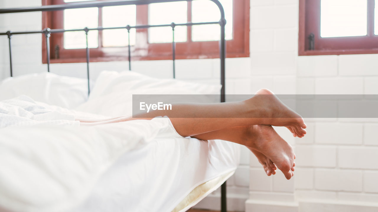 low section of woman relaxing on bed at home