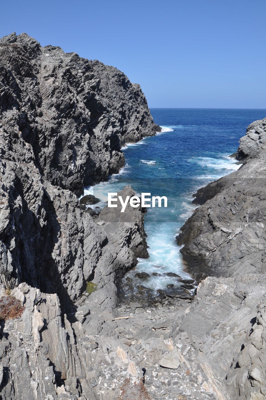 Scenic view of rocks in sea against clear blue sky