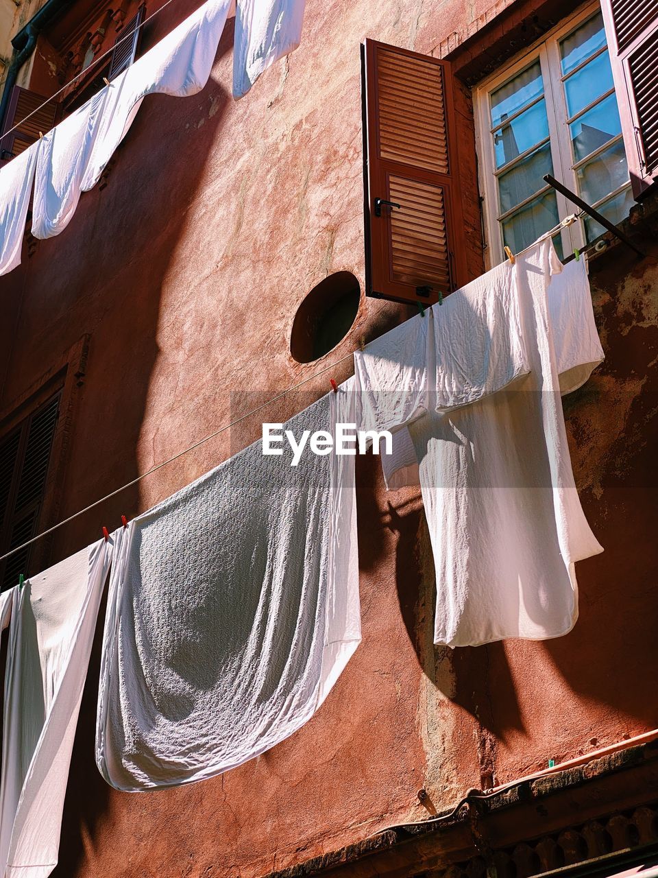 White sheets and clothes hanging and drying against a colorful facade with sunlight and shadows 