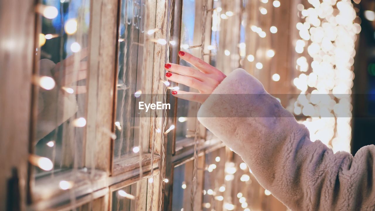 Close-up of woman hand touching illuminated lights on window