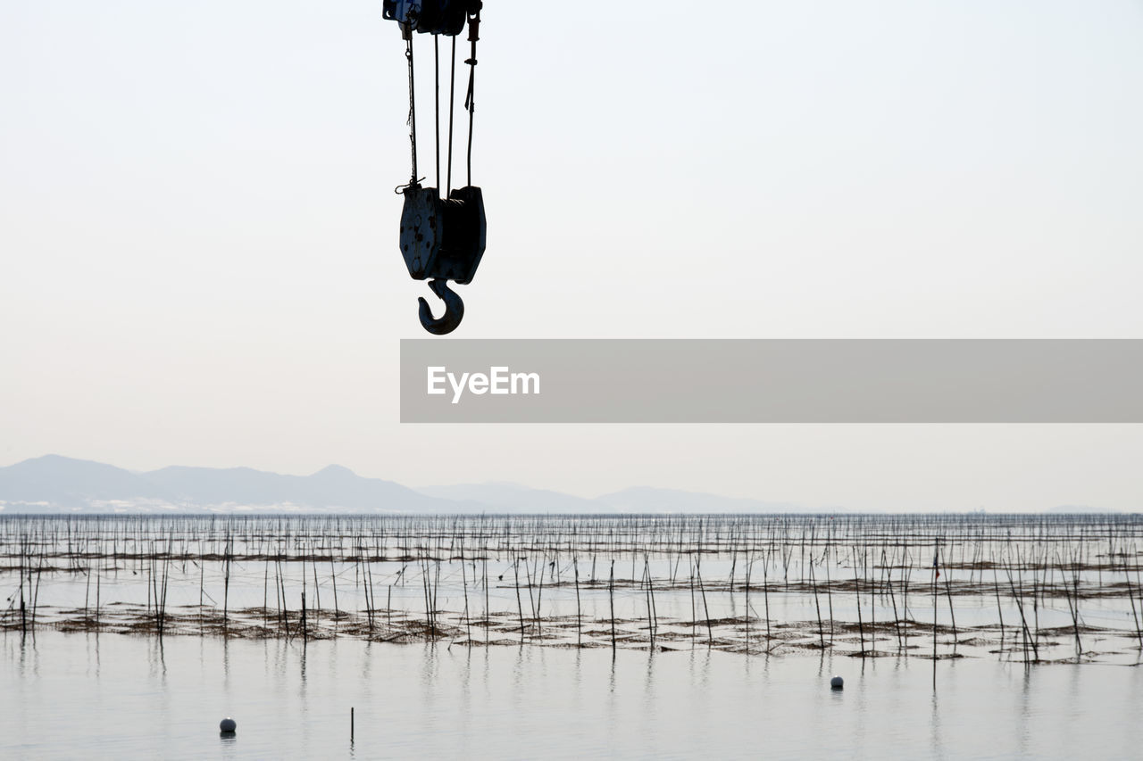 Crane pulley over sea against sky