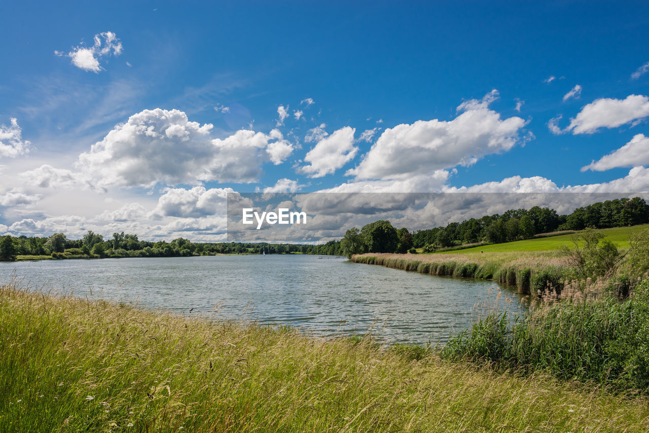 Scenic view of river against cloudy sky on sunny day