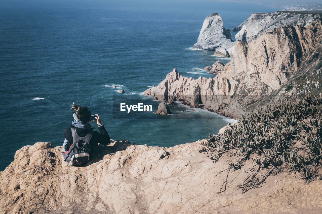 High angle view of woman sitting on rock formation by sea