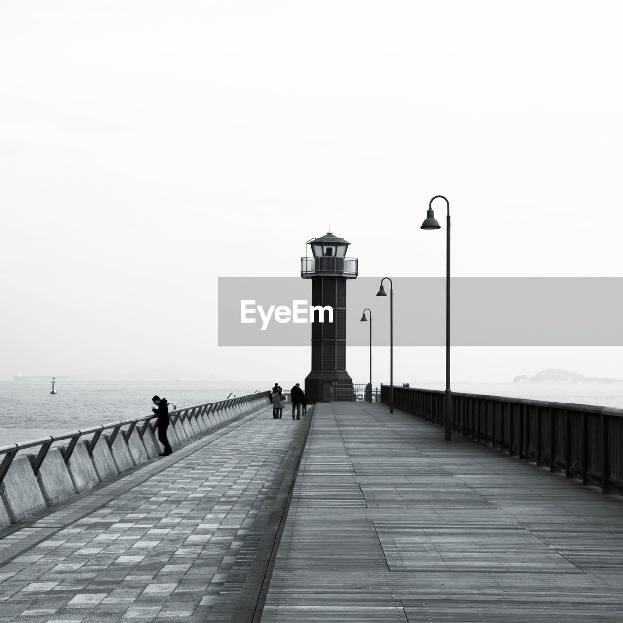 PEOPLE WALKING ON PIER AMIDST SEA AGAINST SKY