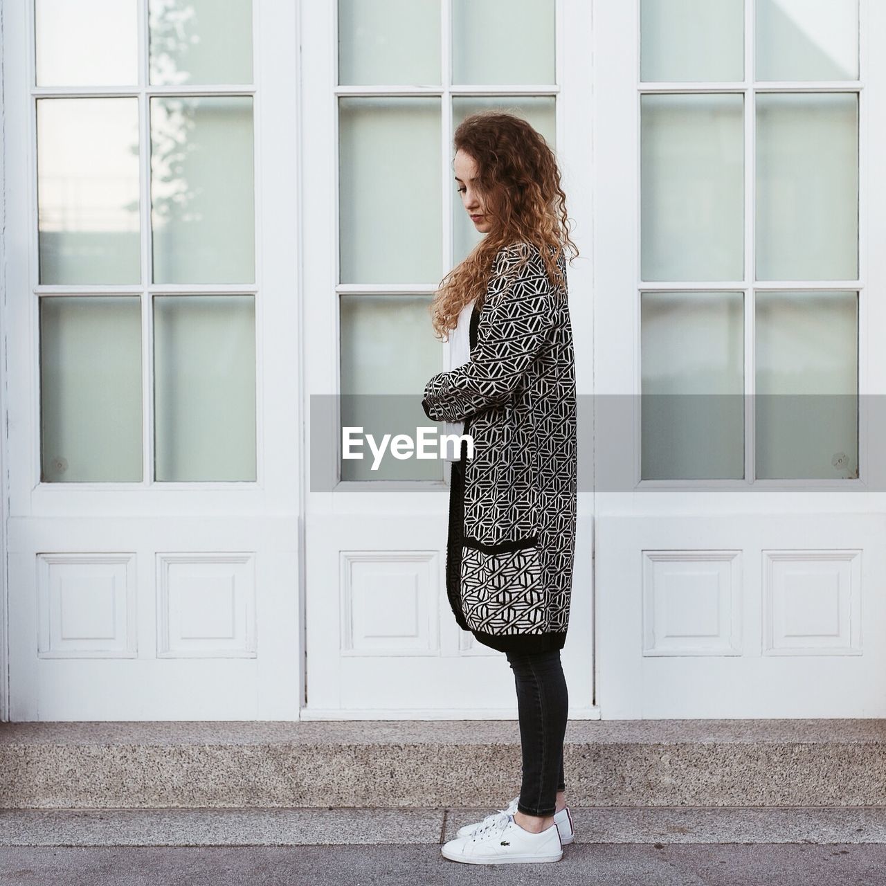 Side view of beautiful young woman standing on steps outside house