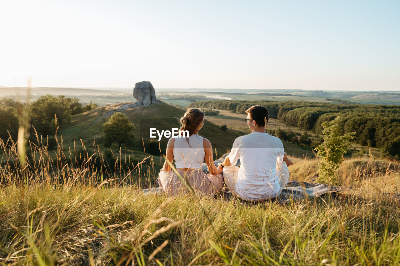 Man and woman practicing yoga and meditation outdoors at sunset with scenic landscape
