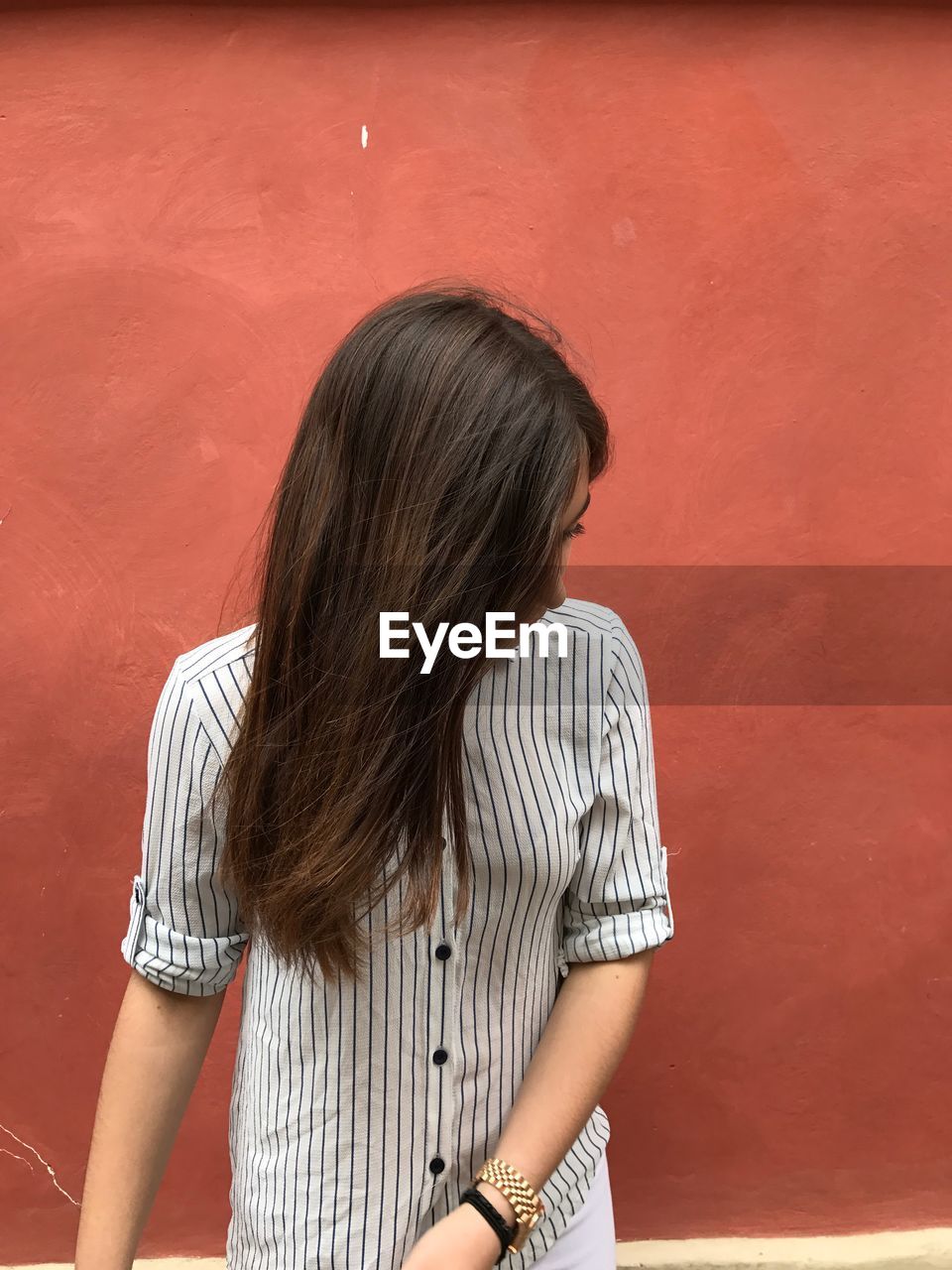 Teenage girl with long hair standing against red wall