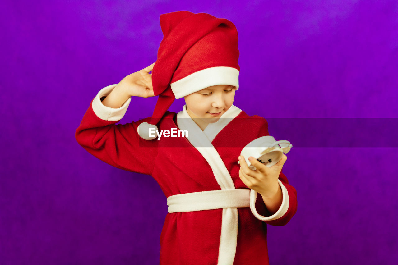 colored background, studio shot, hat, celebration, one person, costume, childhood, child, clothing, indoors, red, cartoon, portrait, happiness, smiling, holding, emotion, christmas, men, dressing up, fun, waist up, event, standing, performing arts, holiday, adult