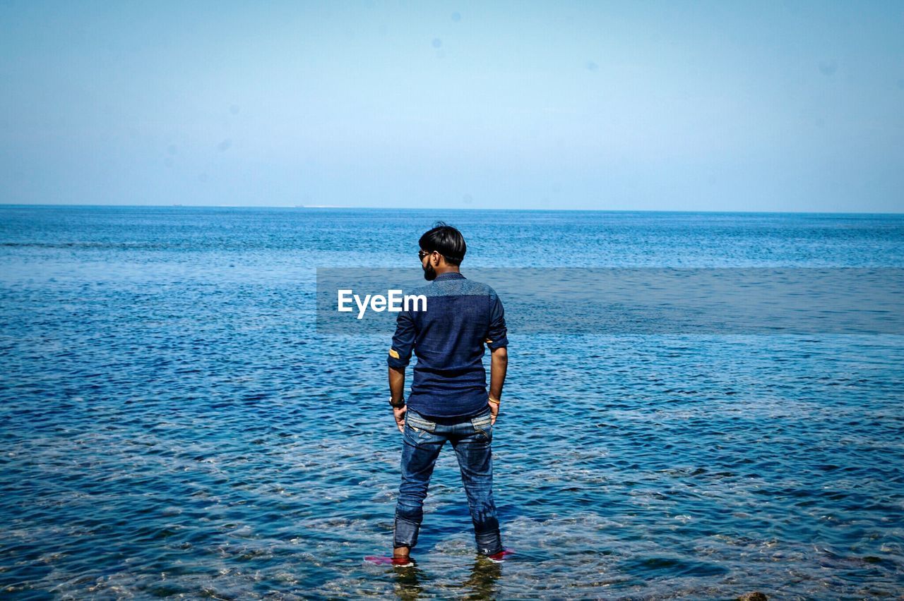 Rear view of man standing in sea against sky