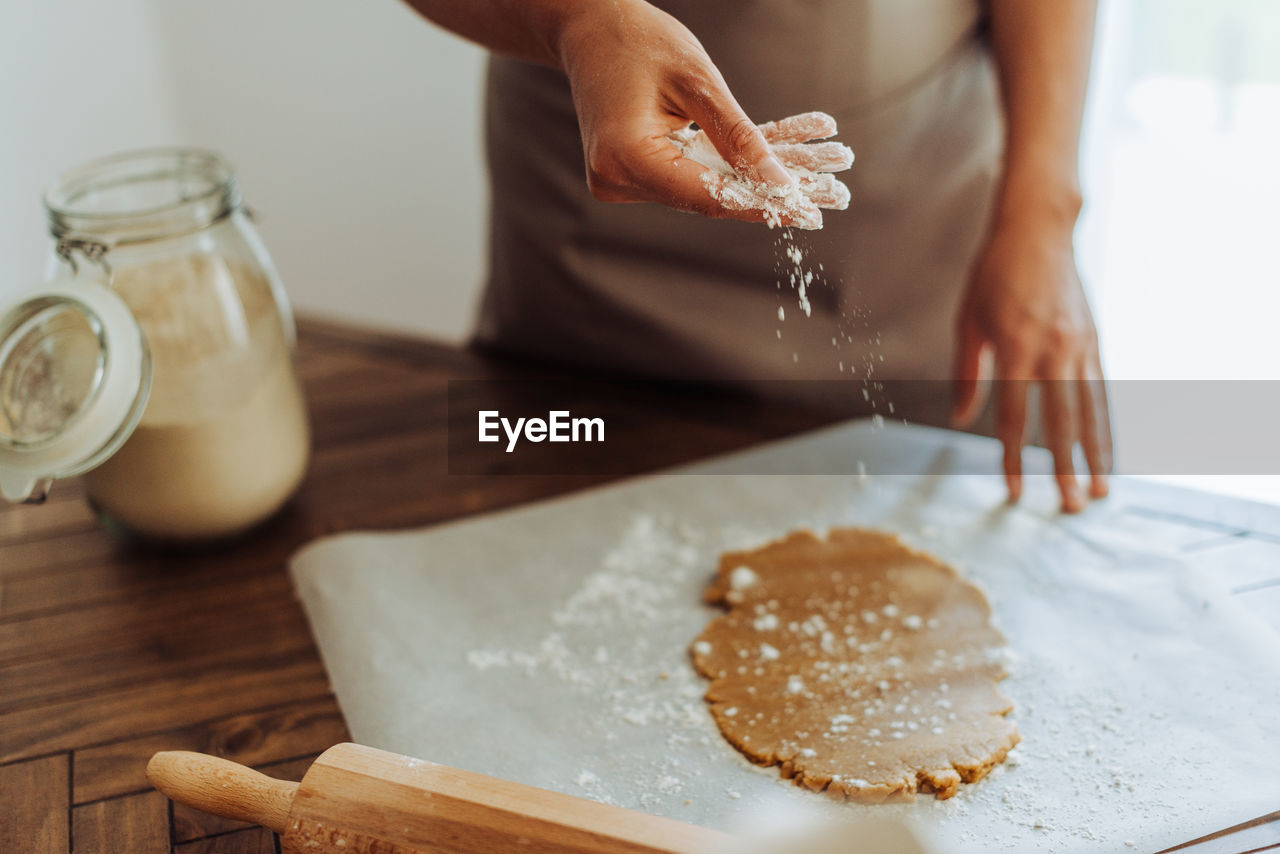 Midsection of a woman sprinkling flour on dough while making cookies