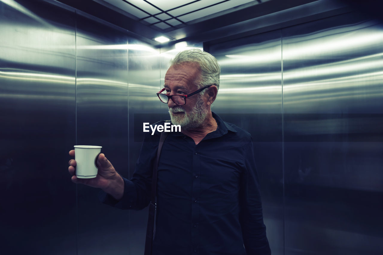 Man holding coffee cup while standing in elevator