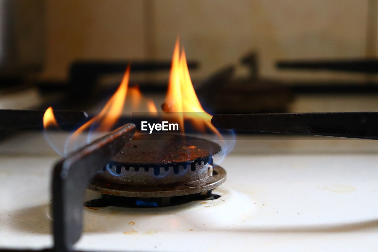 Picture of old and dirty black gas stove burner with blue and orange flames burning for cooking.
