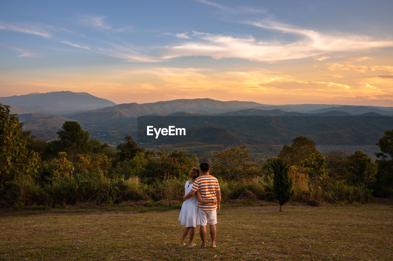 REAR VIEW OF WOMAN AGAINST MOUNTAINS AGAINST SKY